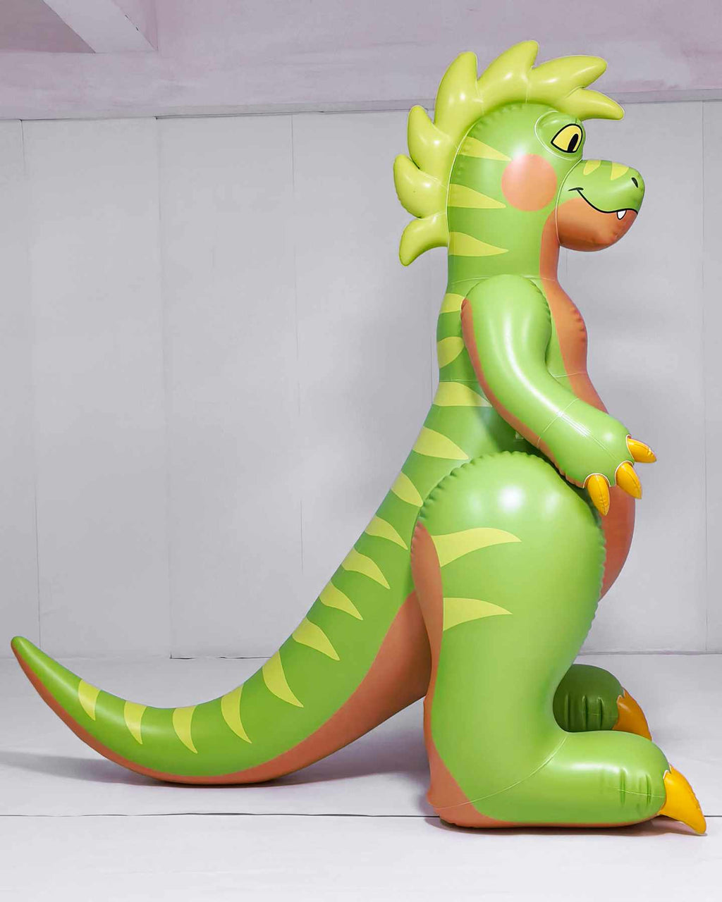 Raptary is a green inflatable dinosaur toy. Made by Jet Creations and Rapatary. Sold by SqueakClub. This is a side view of Raptary. Raptary is 6 feet tall. You can see its long tail, striped back, and wavy hair crest. It stands on two feet with its tail on the ground.